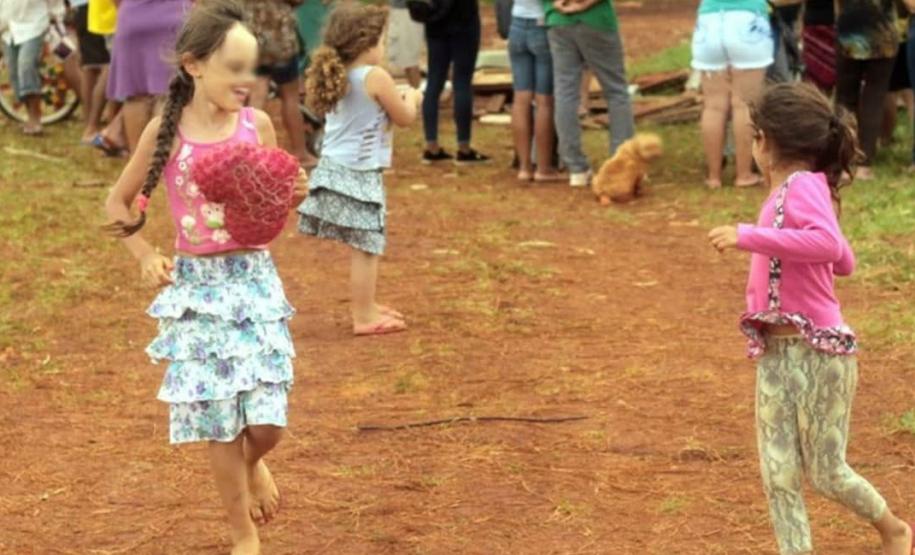 Crianças brincando, enquanto os moradores estão reunidos ao fundo.
