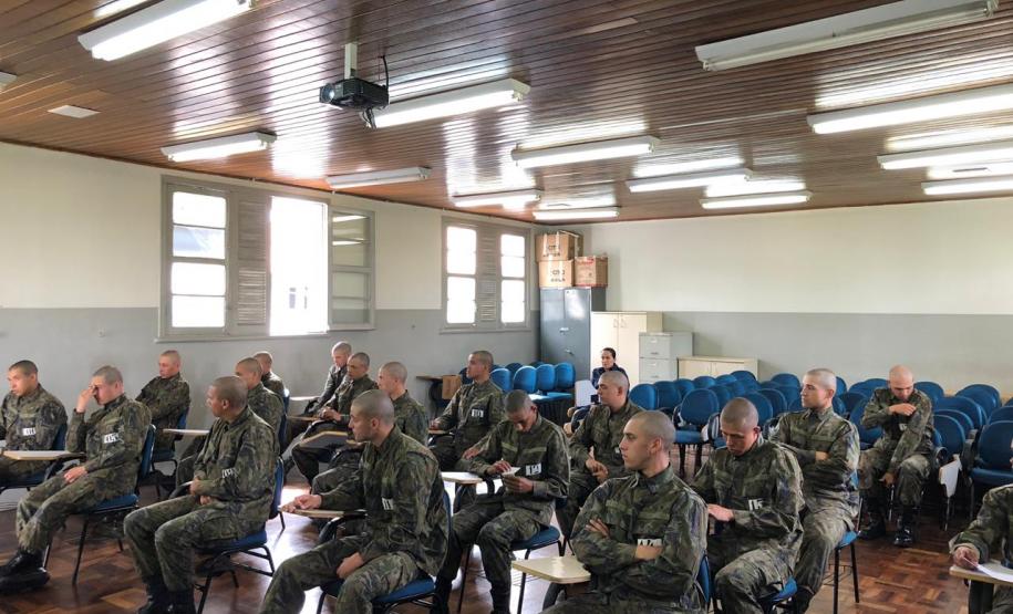 A imagem foi tirada na parte da frente focando nos alunos. Vemos esses prestando atenção na equipe da DPPR que está fora do quadro da imagem.