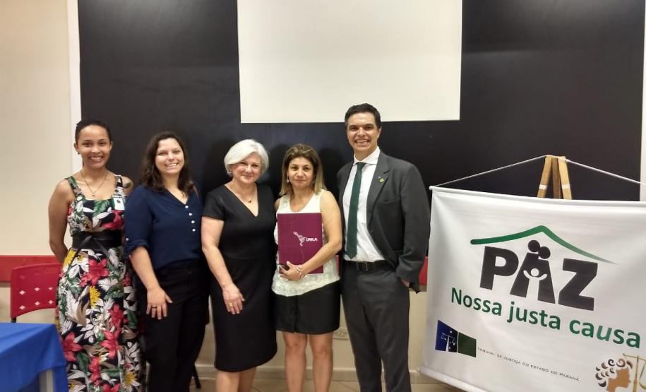 Equipe Técnica da DPPR participa da campanha “Semana da justiça pela paz em casa” em Foz do Iguaçu Na imagem vemos a Equipe Técnica da DPPR juntos, posando para a foto, do lado de um cartaz do evento.