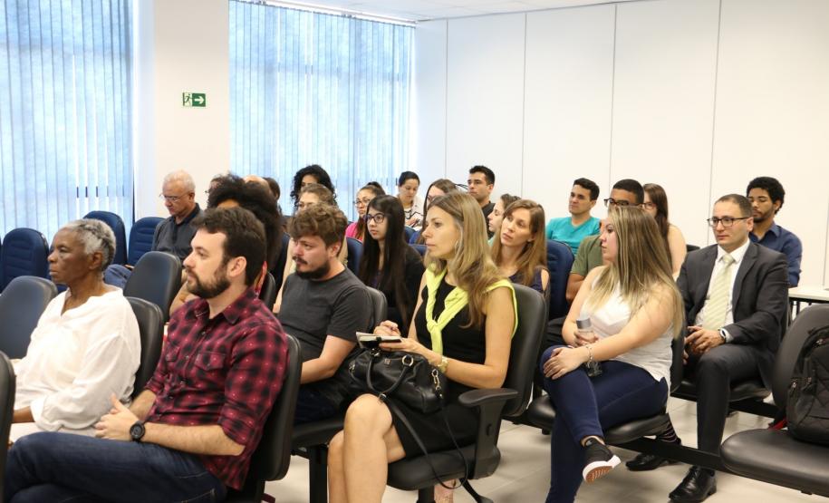 Na imagem vemos o público do evento, estão todos sentados, prestando atenção em algo que lhes é dito/mostrado a sua frente.