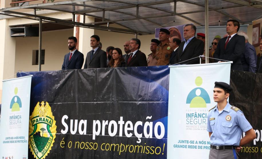 Palanque do evento com convidados na parte de cima da foto. Na parte de baixo, na direita, um aluno do Colégio Militar.