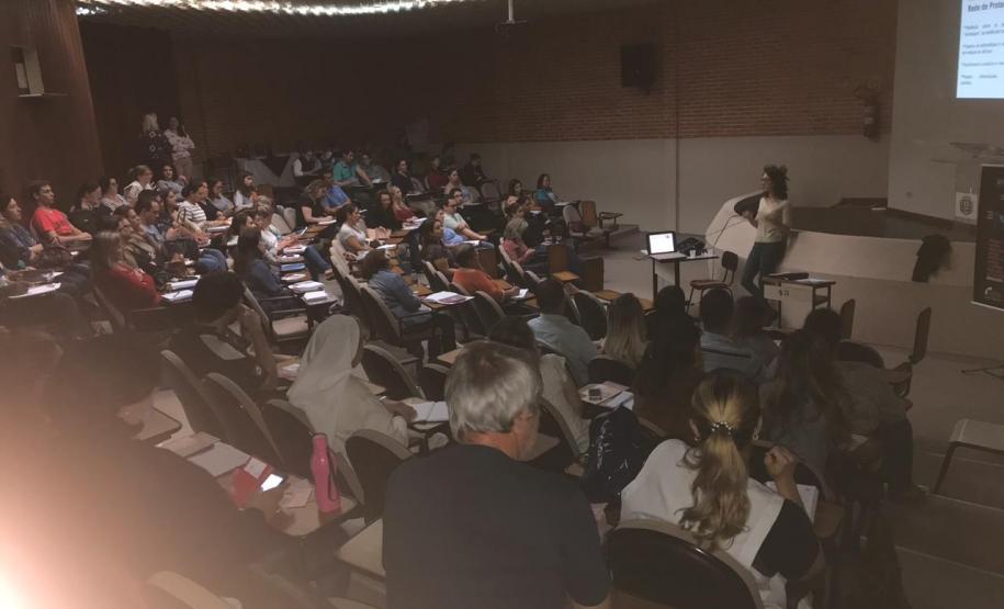 Imagem tirada durante uma palestra. Mostra uma palestrante de frente para o público.