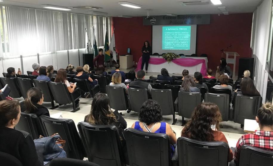 NUDEM palestra na Polícia Civil Imagem tirada durante a palestra do funda da sala. Vemos as costas dos ouvintes e a palestrante a frente.