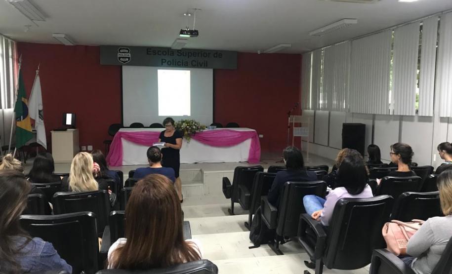 NUDEM palestra na Polícia Civil Imagem também tirada durante a palestra do funda da sala. Vemos as costas dos ouvintes e a palestrante a frente.