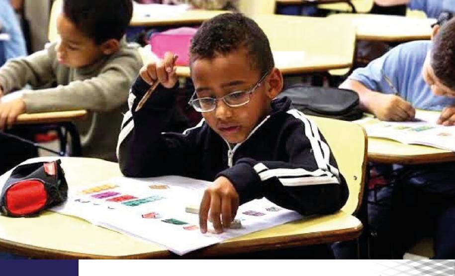 #LegendaAcessi&#769;vel: A imagem apresenta crianças na sala de aula, com um aluno concentrado no seu dever, em destaque no primeiro plano.

No rodapé, no canto esquerdo a data 25 Agosto, Dia Nacional da Educação Infantil e no canto direito, a logo da DPE-PR