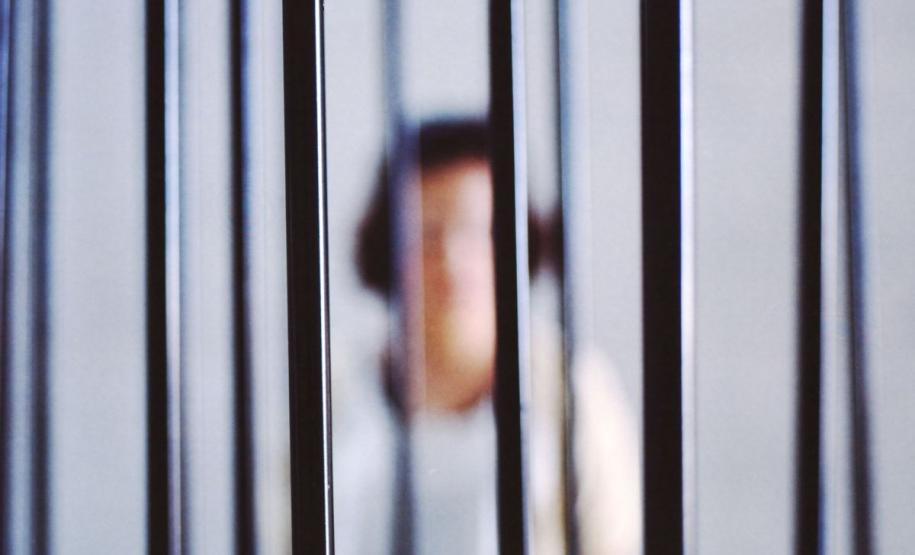 DPE-PR garante medidas adequadas no Complexo Médico Penal #LegendaAcessível: Uma foto desfocada de uma mulher atrás das grades.