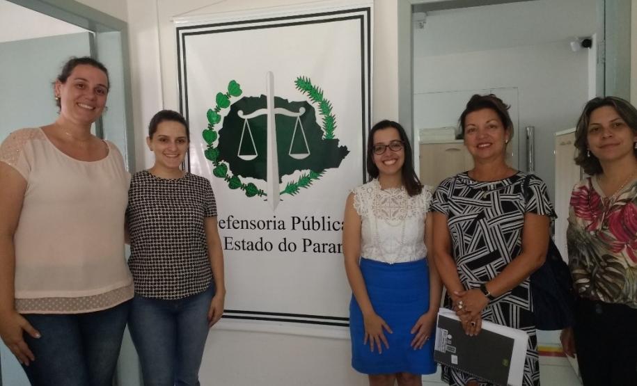 Defensoria Pública em Campo Mourão realiza reunião com a Secretaria de Ação Social Da esquerda para a direita: Thaís Fondazzi Radecki, Tânia Cordeiro Aldivino, Mariana Gonzaga Amorin, Fabrícia Bronzel e Silvia Andreia Rocha. Legenda acessível: Na imagem estão as participantes olhando para a foto e sorrindo. Estão ao lado de um banner com a logo da defensoria, estão duas para a esquerda e três para a direita.